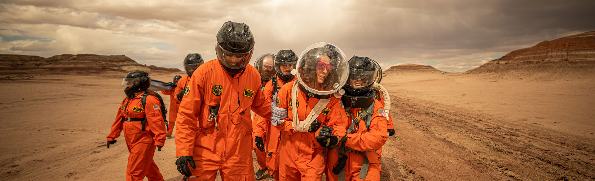 Students and instructors clad in orange space suits and space helmets train in desert