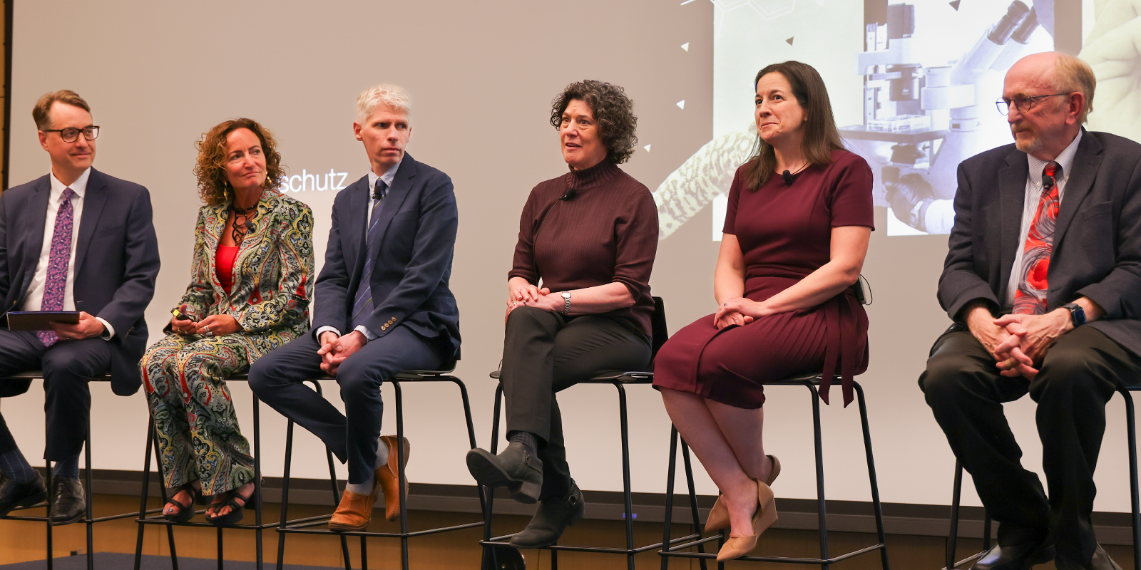 Six participants lined up in chairs on stage for a Q and A.