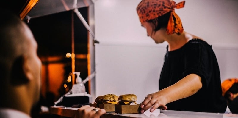 Food truck worker handing cheeseburgers to a customer.