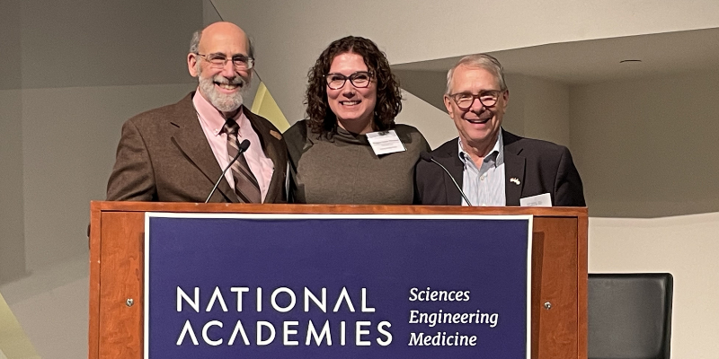 Image of three individuals smiling behind a podium.
