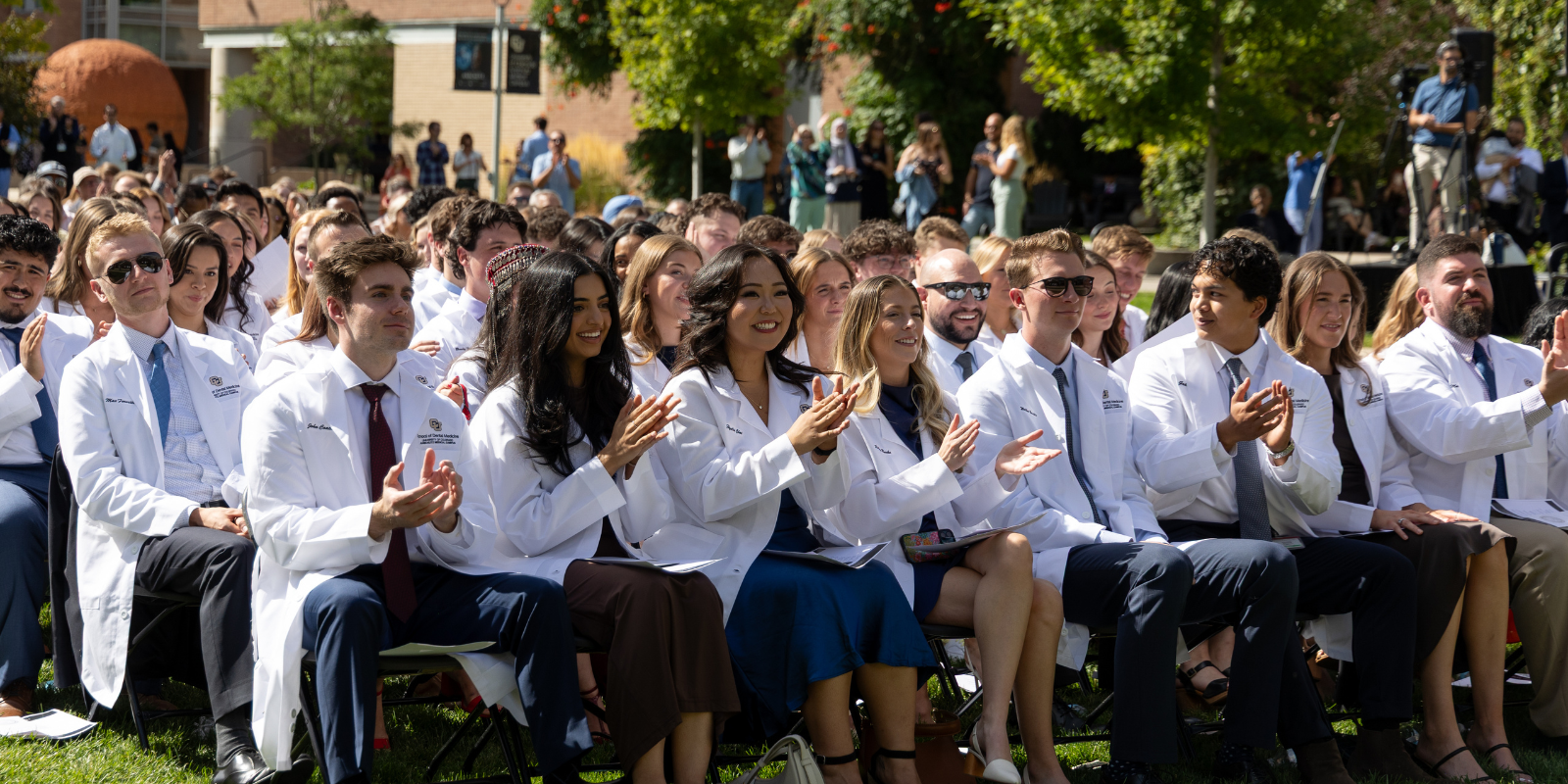 dental students in their white coats clapping, seated 