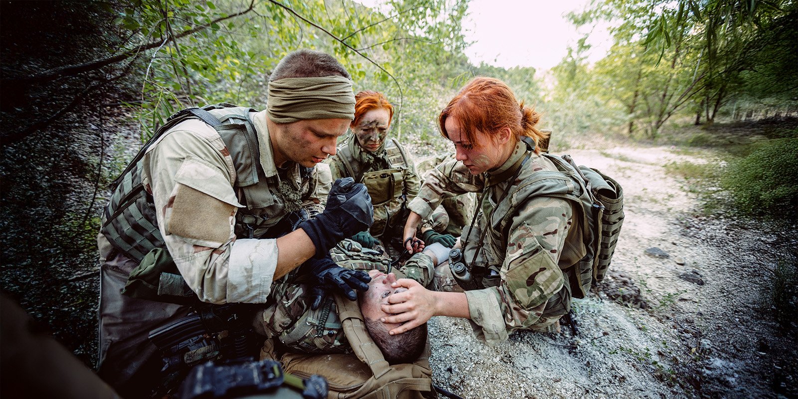 Three military students participating in a medical training exercise examine an injured actor for triage