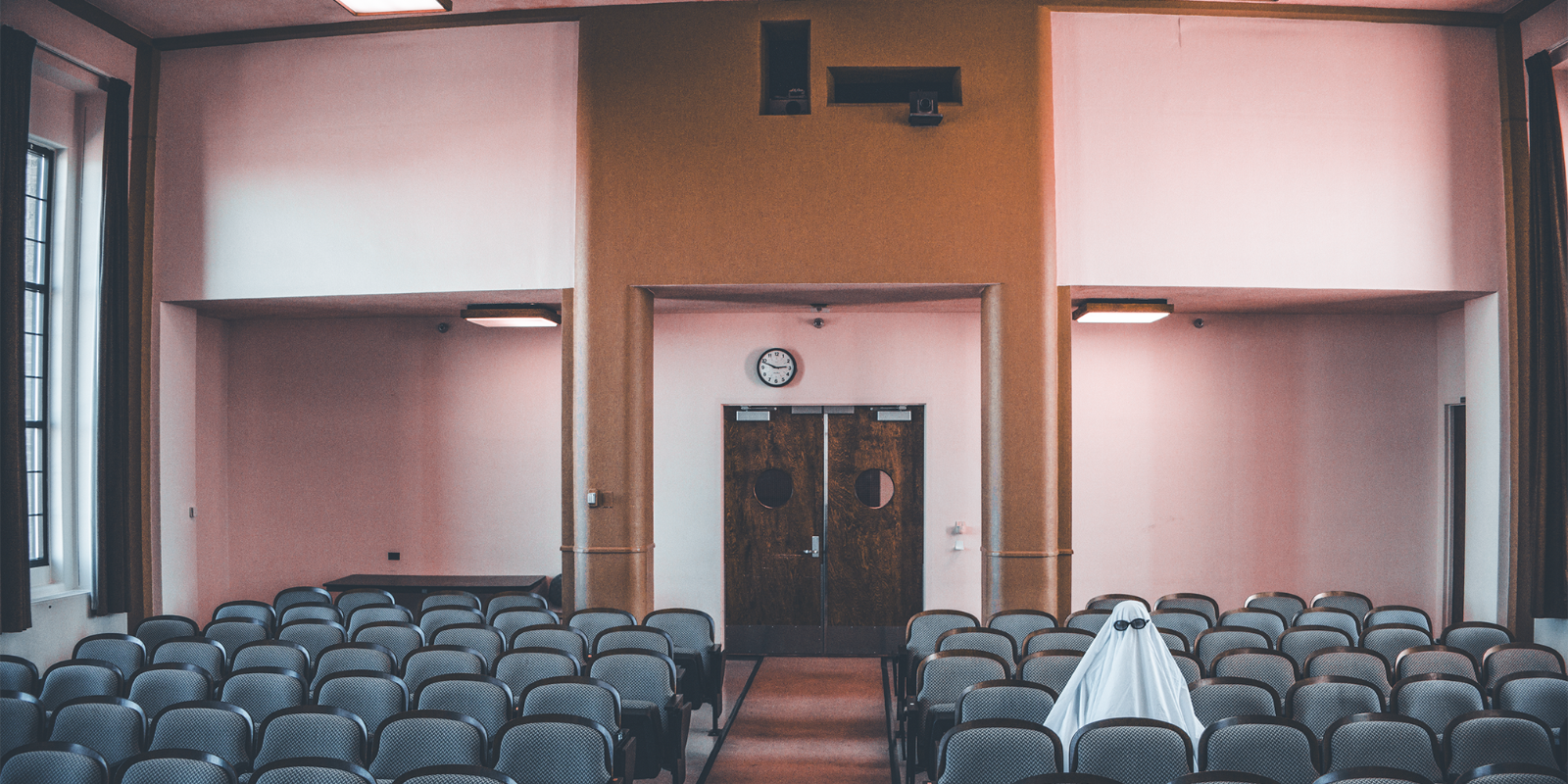 A "ghost" sits in Bushnell Auditorium facing stage, with view of projector room windows