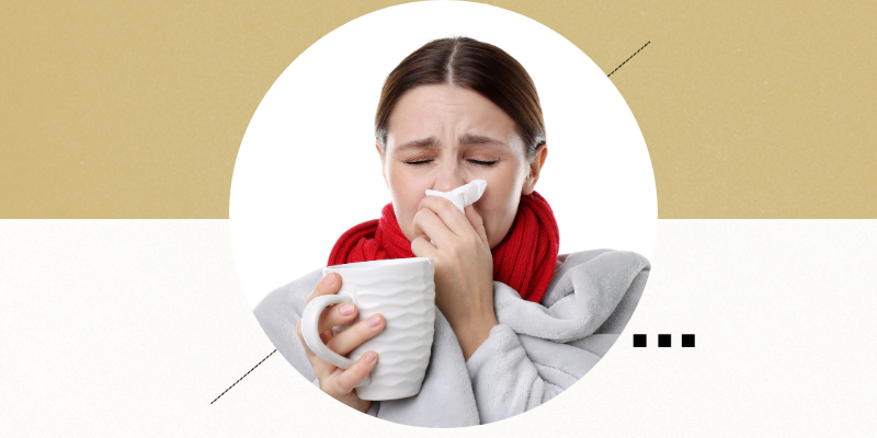 A woman blowing her nose and holding a mug