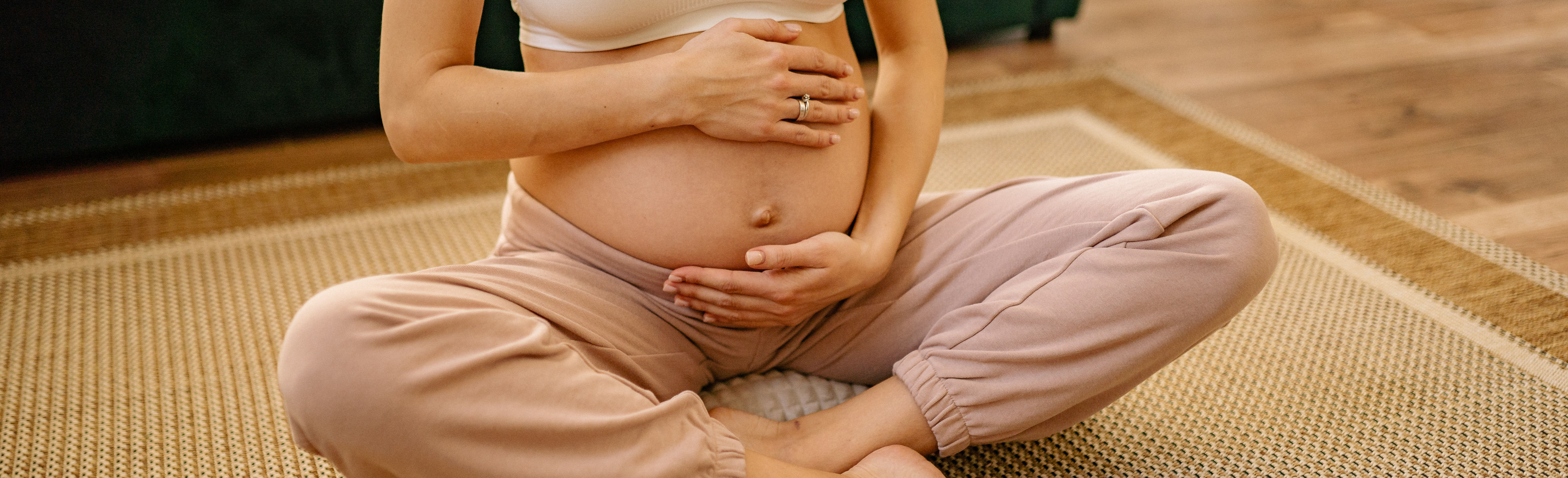 pregnant woman seated on floor cradling stomach in hands