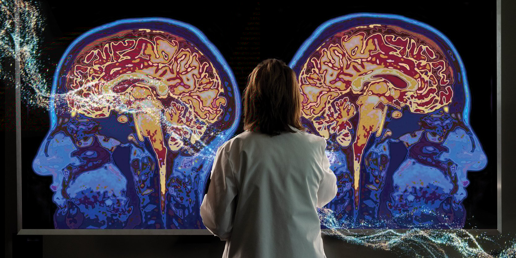 A doctor stands in front of a wall displaying two images of brain scans. 