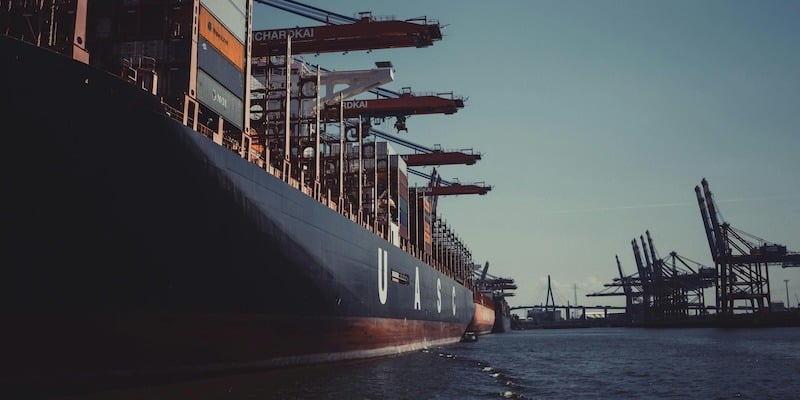 Header picture of a barge shipping boat with lots of shipping containers.