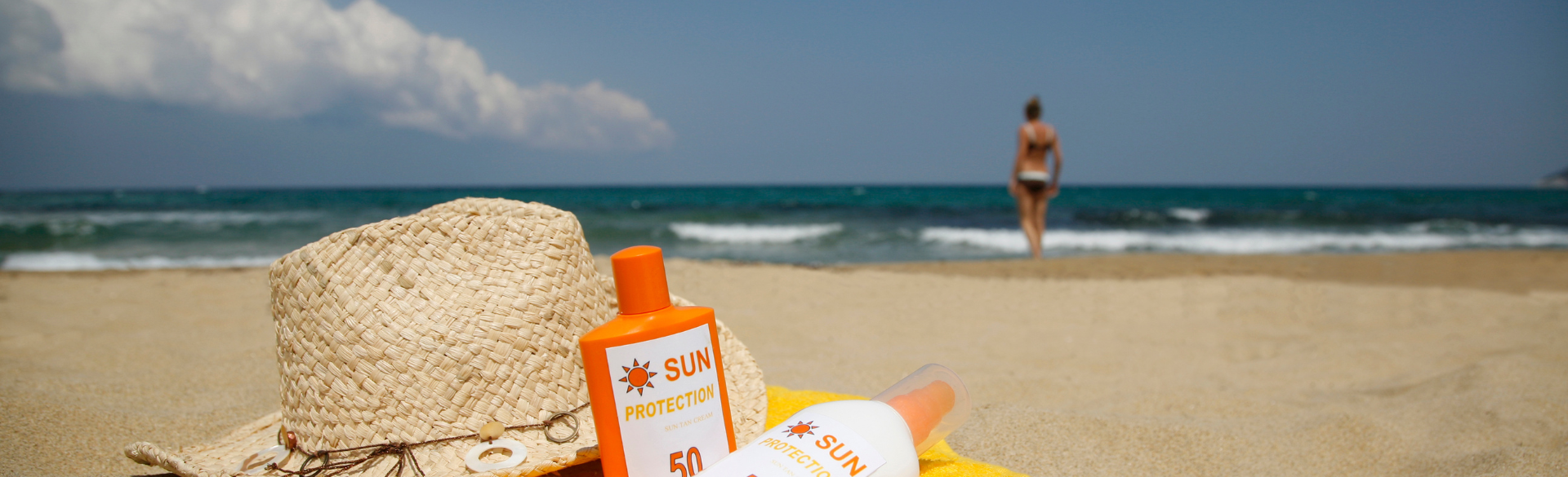 Sunscreen and sun hat on a beach with person in background